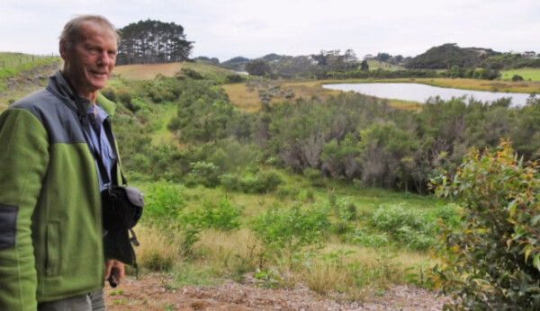 A man stands in a scrubby landscape near a lake