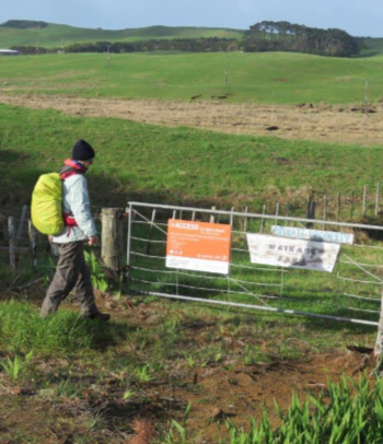 A walker approaches a farm gate with access signage on it.